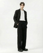 Tall men's black crinkle pants layered with long coat, editorial styling

