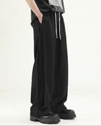 Tall men's black pleated wide leg pants, side profile highlighting wide leg opening and fabric drape