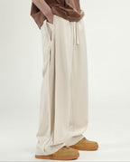 Tall men's cream pleated wide leg pants, front view highlighting pleat detail and relaxed wide silhouette