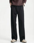 Tall men's black relaxed pleated trousers, front view highlighting pleat detail and straight silhouette
