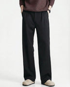 Tall men's black relaxed pleated trousers, front view highlighting pleat detail and straight silhouette