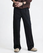 Black relaxed pleated trousers for tall men, full-length side view with casual white sneaker styling
